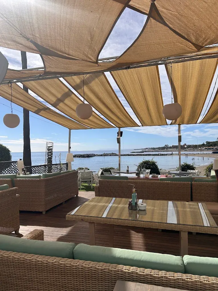 Wicker lounge seating and a timber table under the sails, the sea beyond