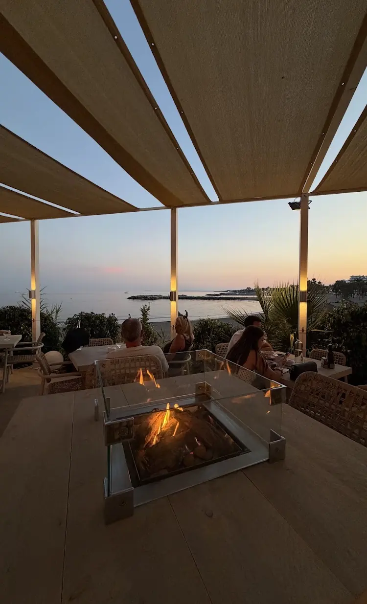 Dusk on the terrace: a glass fire table glowing, guests at their tables and the sea fading to pink