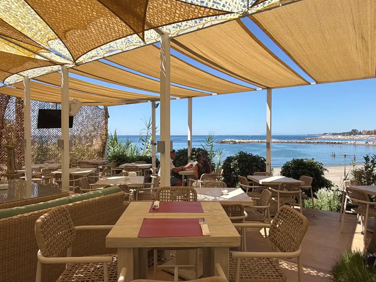 The shaded terrace at Relais de Paris, tables set with red placemats, looking out over the beach and the sea at Puerto Banús